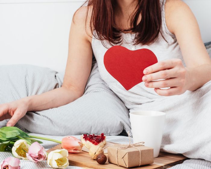 The girl is holding a red heart. Congratulations on Valentine's Day on February 14. Breakfast in bed and a gift