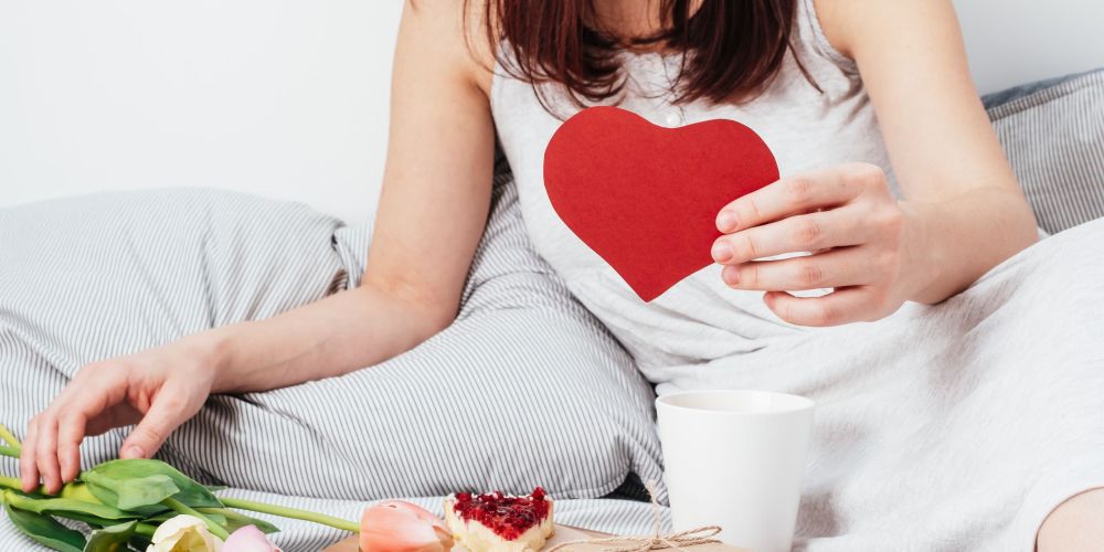 The girl is holding a red heart. Congratulations on Valentine's Day on February 14. Breakfast in bed and a gift