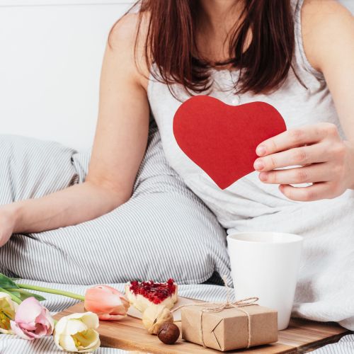 The girl is holding a red heart. Congratulations on Valentine's Day on February 14. Breakfast in bed and a gift
